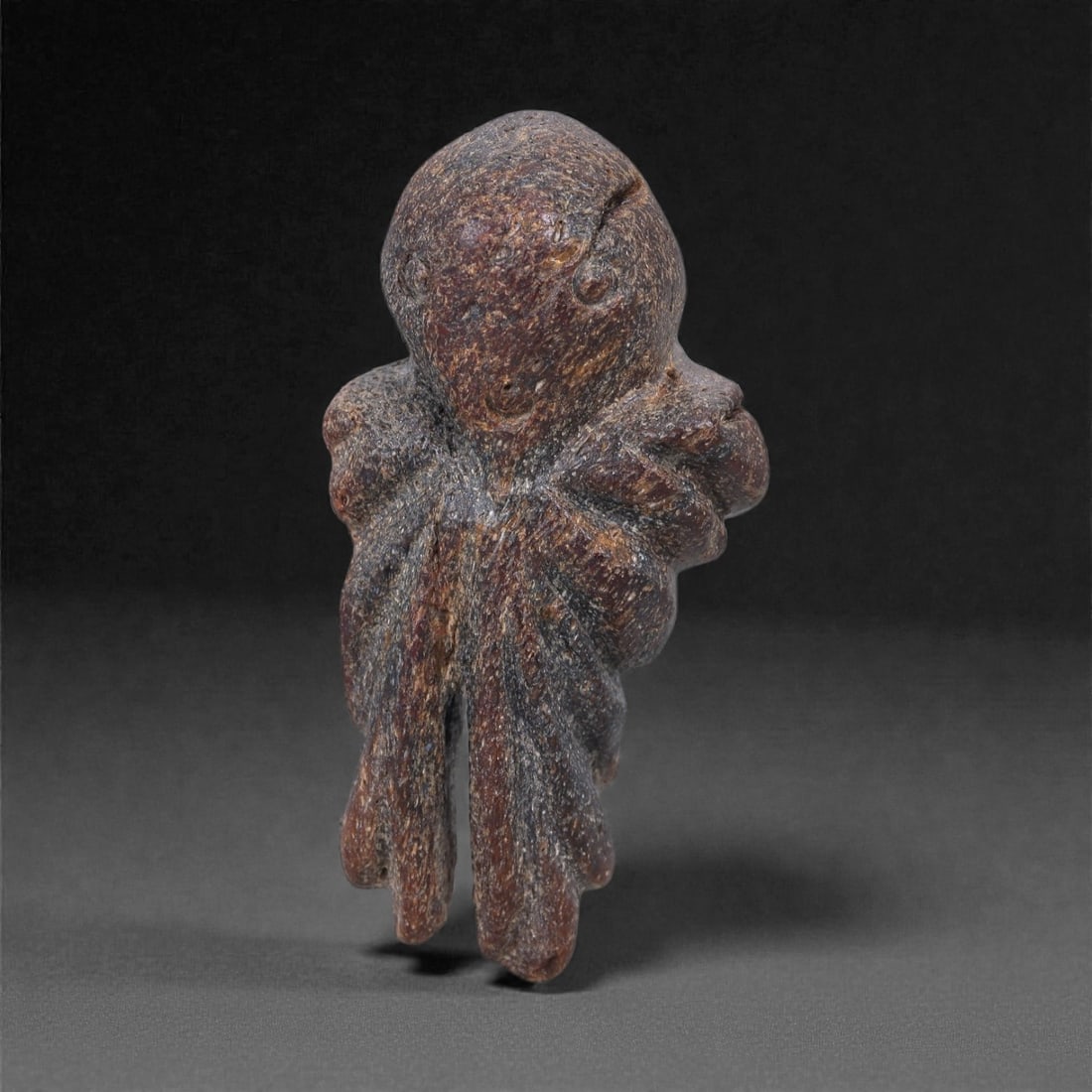 A Near Eastern Stone Anthropomorphic Figurine, 4th-3rd Millennium BCE, 2E: Carved from a dense brown stone with fine granular texture and darker mineral inclusions, the object represents a highly schematic standing anthropomorphic figure. The head is rounded and disproportio
