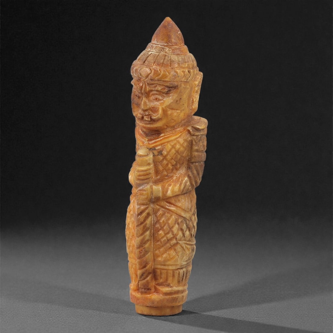 An Indo-Himalayan Bone Carved Finial, 20th Century, 22LS: Carved from warm-toned bone with natural mottling, the finial takes the form of a standing guardian figure holding a vertical staff. The head is modeled with angular facial features, pronounced brows,