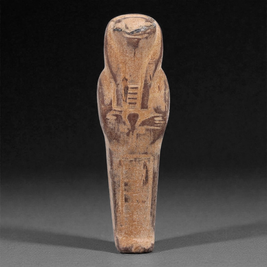 Egyptian Revival Stone Idol - Mummiform Figure, 88F: Carved from a warm brown stone, this mummiform figure is rendered in a slender frontal form with a rounded head, simplified facial plane, and schematically carved arms folded across the torso, reflect
