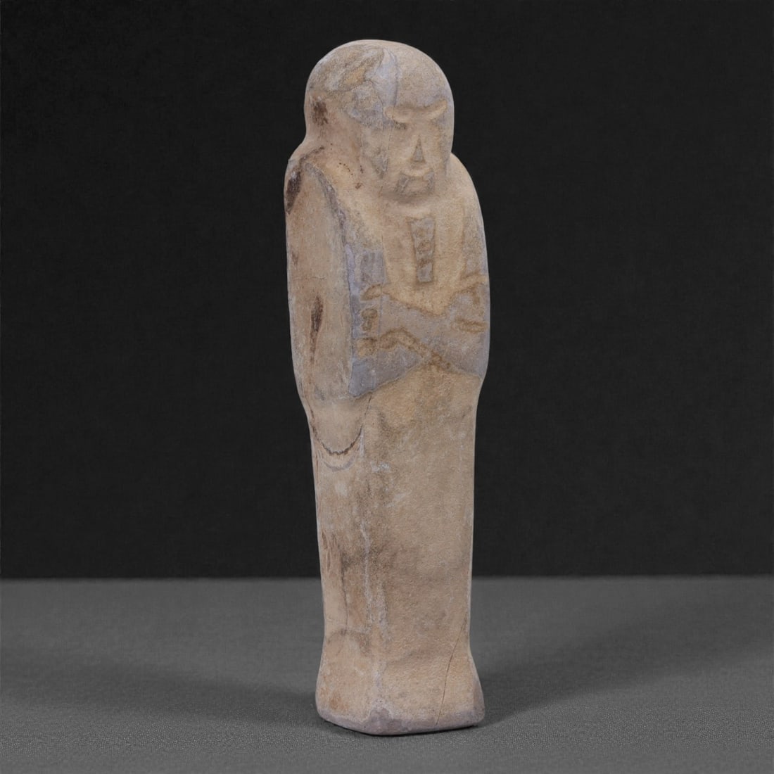 Egyptian Revival Stone Idol - Mummiform Figure, 100G: Carved from a pale beige stone with subtle grey veining, this mummiform figure is rendered in a frontal, elongated form with a rounded head, simplified facial features, and arms schematically folded a