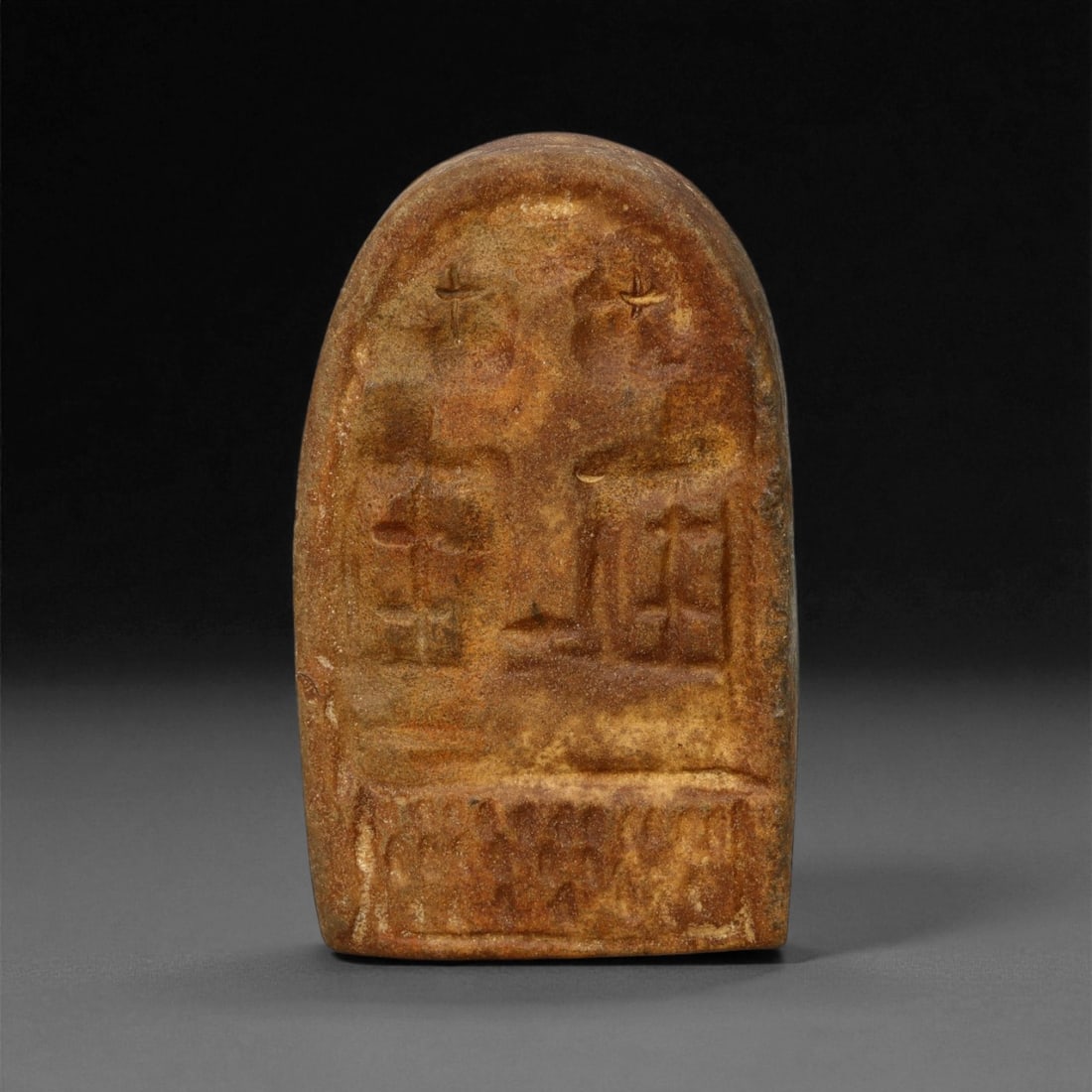 A Late Antique Stone Christian Stela, 4th-7th Century CE, 76LA: Carved from a brown stone with a slightly granular surface, the stela is shaped with a rounded upper edge and a flat reverse. The front bears shallow relief decoration organized in two zones: in the u