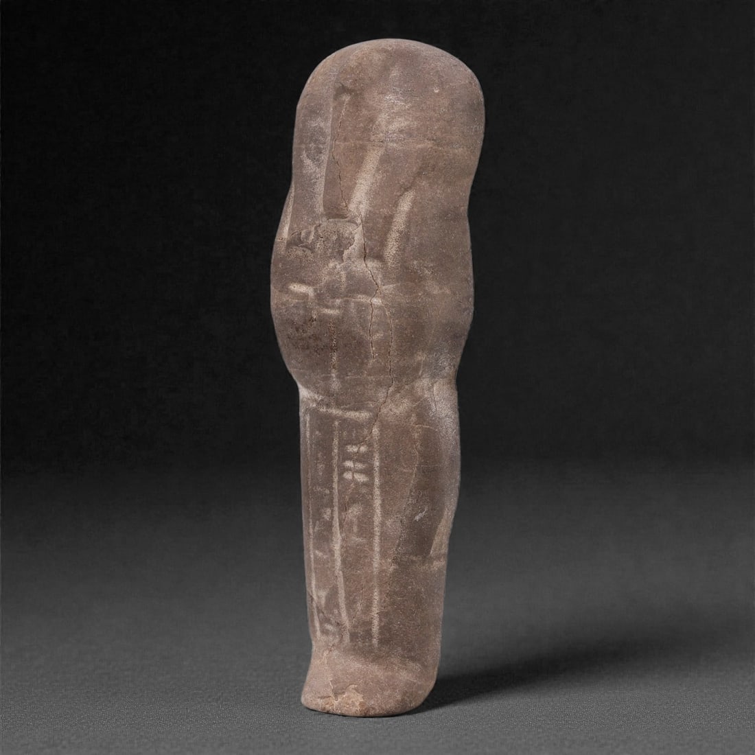 Egyptian Revival Stone Idol - Mummiform Figure, 14G: Carved from a dense brown stone, this mummiform figure is rendered in a simplified, elongated form with gently rounded head and schematically indicated body details, reflecting revivalist interpretati