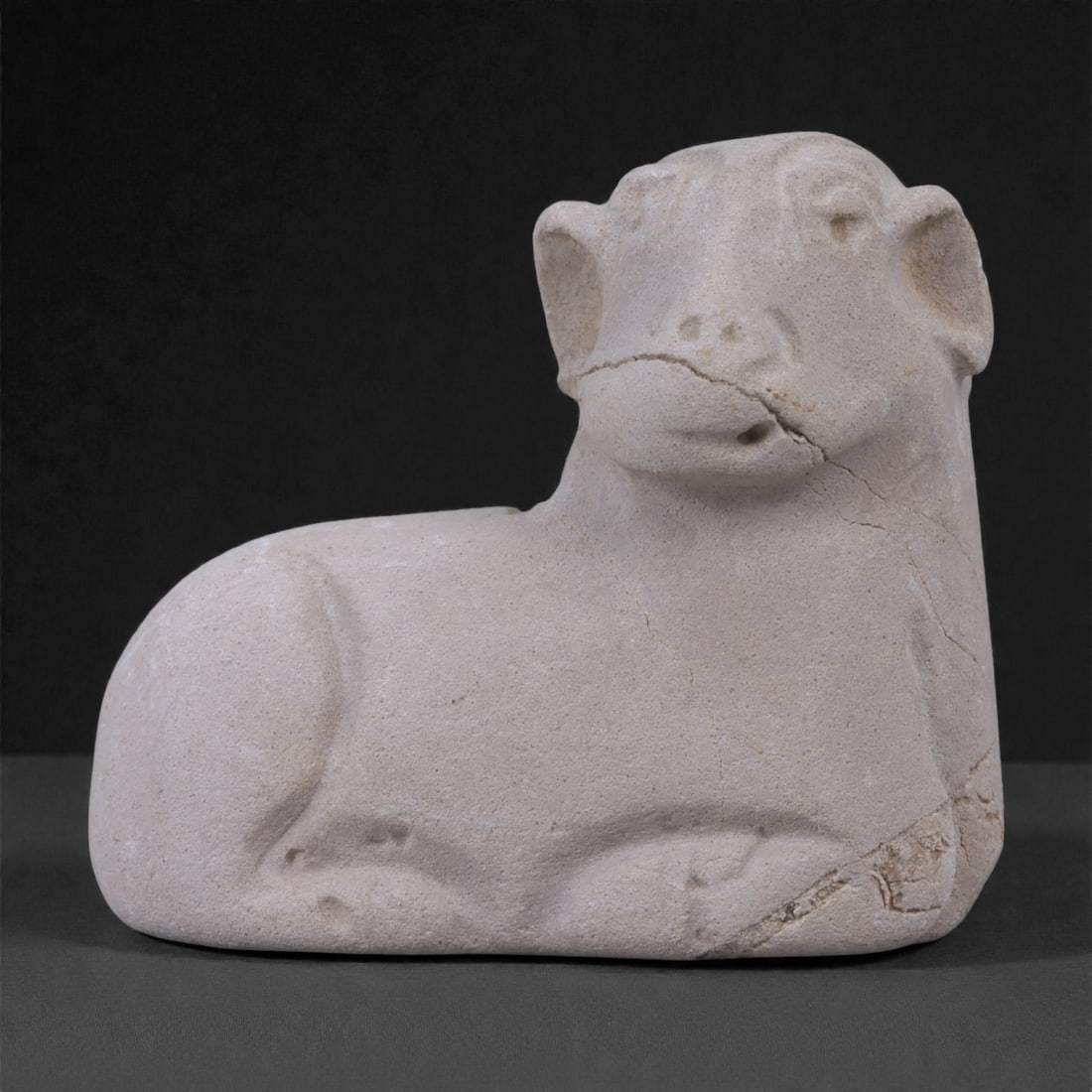 A Near Eastern Stone Zoomorphic Recumbent Bovine Figurine, 3rd-2nd Millennium BCE, 23ZE: Carved from a pale buff to light beige stone with a fine, granular texture, this small zoomorphic figurine depicts a recumbent bovine rendered in a restrained and highly abstracted manner. The animal