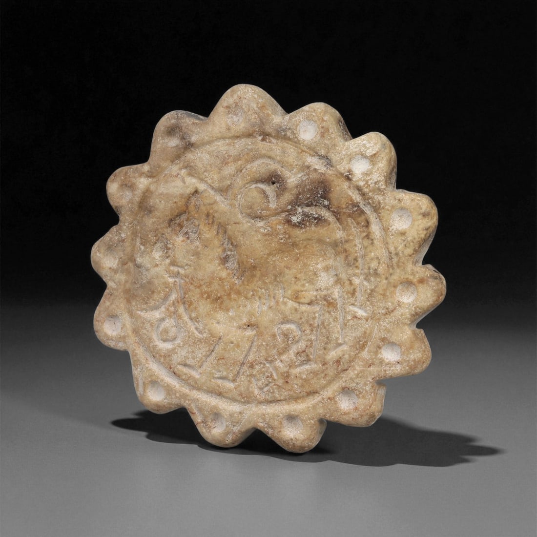 An Indo-Parthian Stone Stamp Seal, 1st-3rd Century CE, 21LE: Carved from a light brown stone with scattered surface encrustations, the circular seal has a scalloped perimeter formed by a series of rounded lobes. The central intaglio depicts a profile feline wit