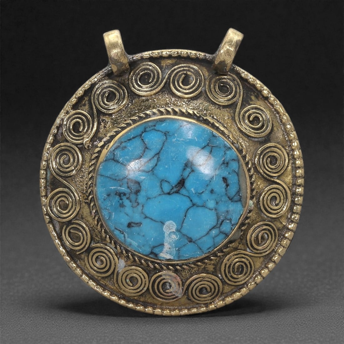 Himalayan Style Brass Pendant - Turquoise Cabochon Spiral, 41XF: This circular brass pendant is centered on a large turquoise cabochon whose rich veining creates a striking visual focus. Surrounding the stone is a textured border followed by a continuous ring of ra