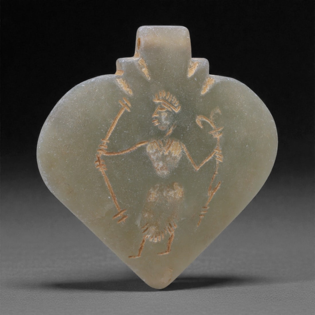 An Eastern Iranian Serpentine Amulet, Islamic Period, 9th-10th Century CE, 5.1cm, 69N: Carved from pale green serpentine with a smooth, slightly translucent surface, the object is worked in low relief on one face, with the reverse left plain and undecorated. The carved elements are defi