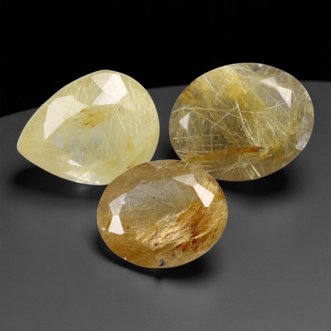 16.84 Carats Golden Rutile Quartz Faceted Trio - Natural 3-Piece Lot, 1.3 to 1.4 cm, 24XE: This captivating trio of golden rutile quartz gems showcases shimmering networks of needle-like inclusions, suspended like golden filaments inside clear to warm-toned quartz bodies. Each stone is face