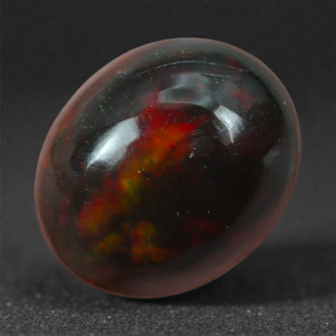1.80 Carats Deep Crimson and Charcoal Black Oval Opal - Natural Welo Origin, 38M: This 10mm oval black opal carries a mysterious, smoldering palette of deep crimson, burnt orange, and shadowy charcoal, with subtle green glints surfacing under bright light. The fire within is subdue