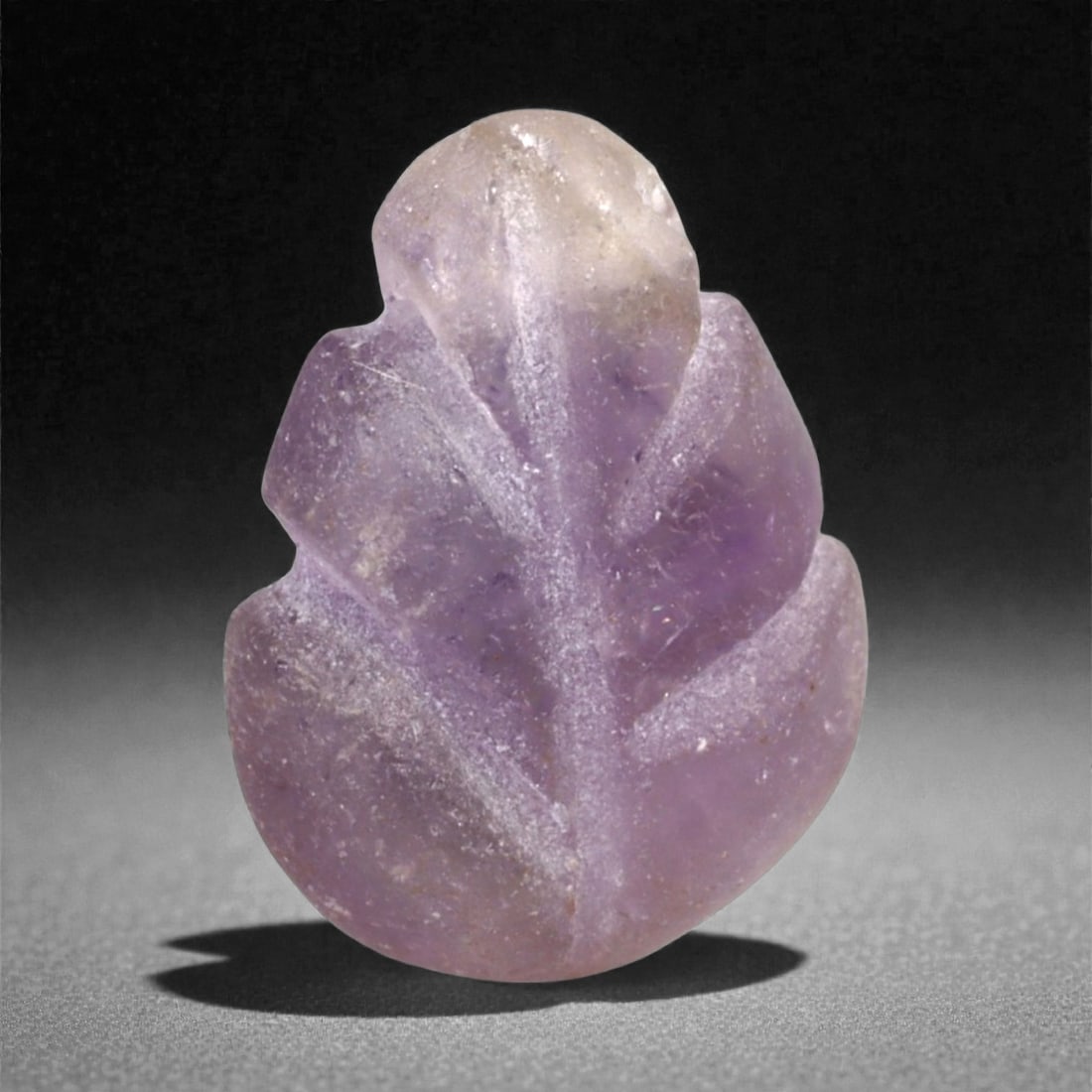 A Medieval Amethyst Carved Leaf Bead, 12th-14th Century CE, 1.2cm, 88LH: Carved from translucent amethyst with areas of surface wear, the bead is shaped as a stylized leaf with incised central and lateral veins. The edges are softly rounded, and a perforation runs vertical