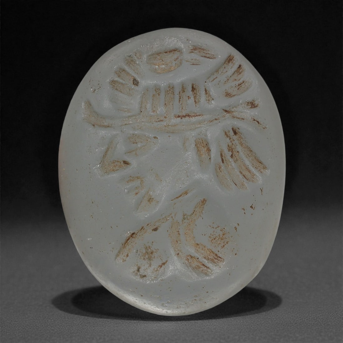 A Sasanian Glass Intaglio, 3rd-7th Century CE, 43LS: Cast from opaque pale grey-white glass, the gem is engraved in intaglio with a schematic composition featuring linear, wedge-shaped, and lobed strokes suggestive of an abstracted anthropomorphic or zo