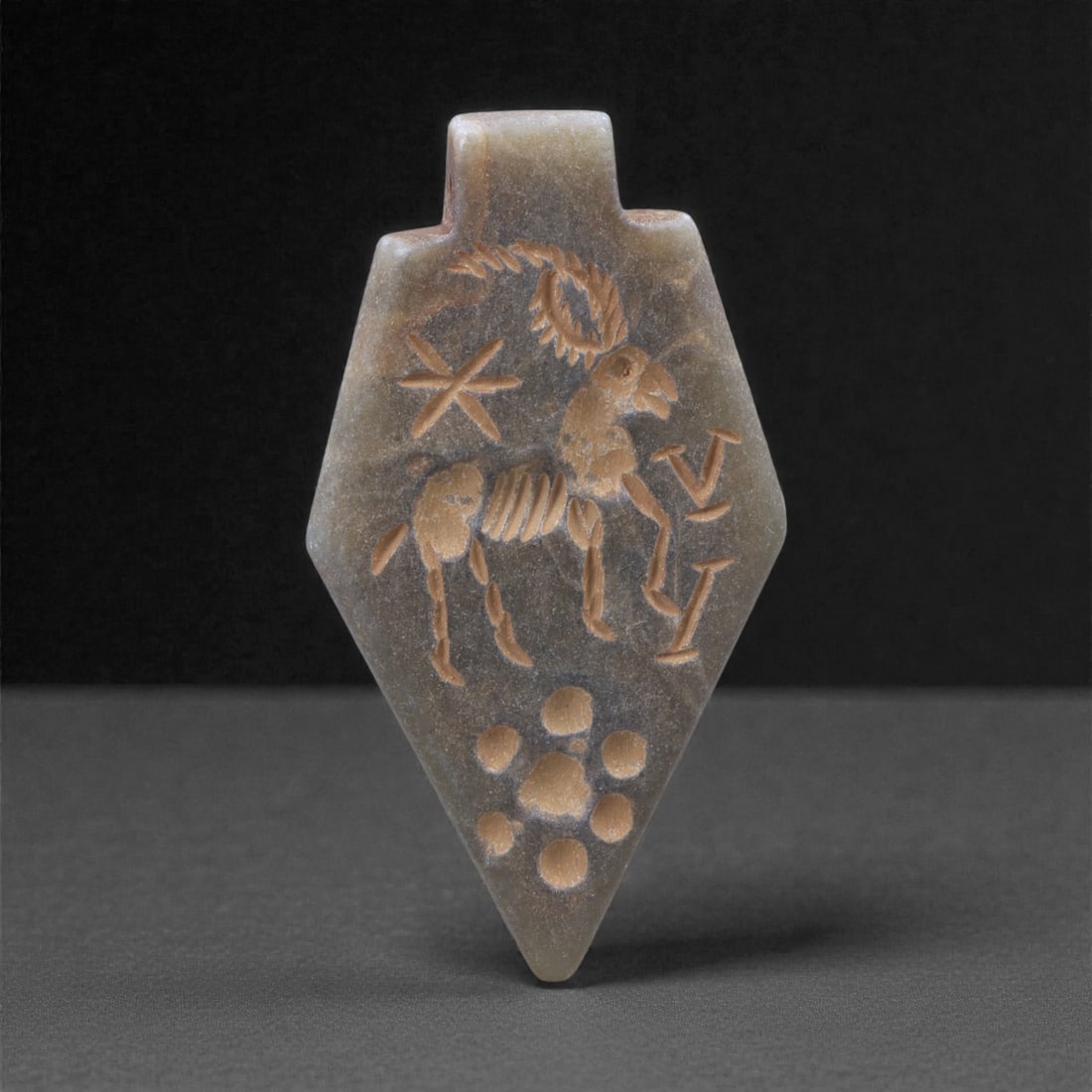 An Eastern Iranian Serpentine Amulet, Islamic Period, 9th-10th Century CE, 4.9cm, 17K: Carved from pale green serpentine with a smooth, slightly translucent surface, the object is worked in low relief on one face, with the reverse left plain and undecorated. The carved elements are defi