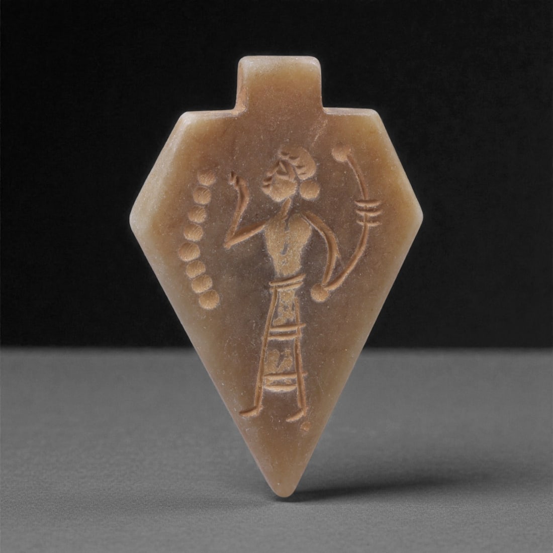 An Eastern Iranian Serpentine Amulet, Islamic Period, 9th-10th Century CE, 4.7cm, 75K: Carved from pale green serpentine with a smooth, slightly translucent surface, the object is worked in low relief on one face, with the reverse left plain and undecorated. The carved elements are defi