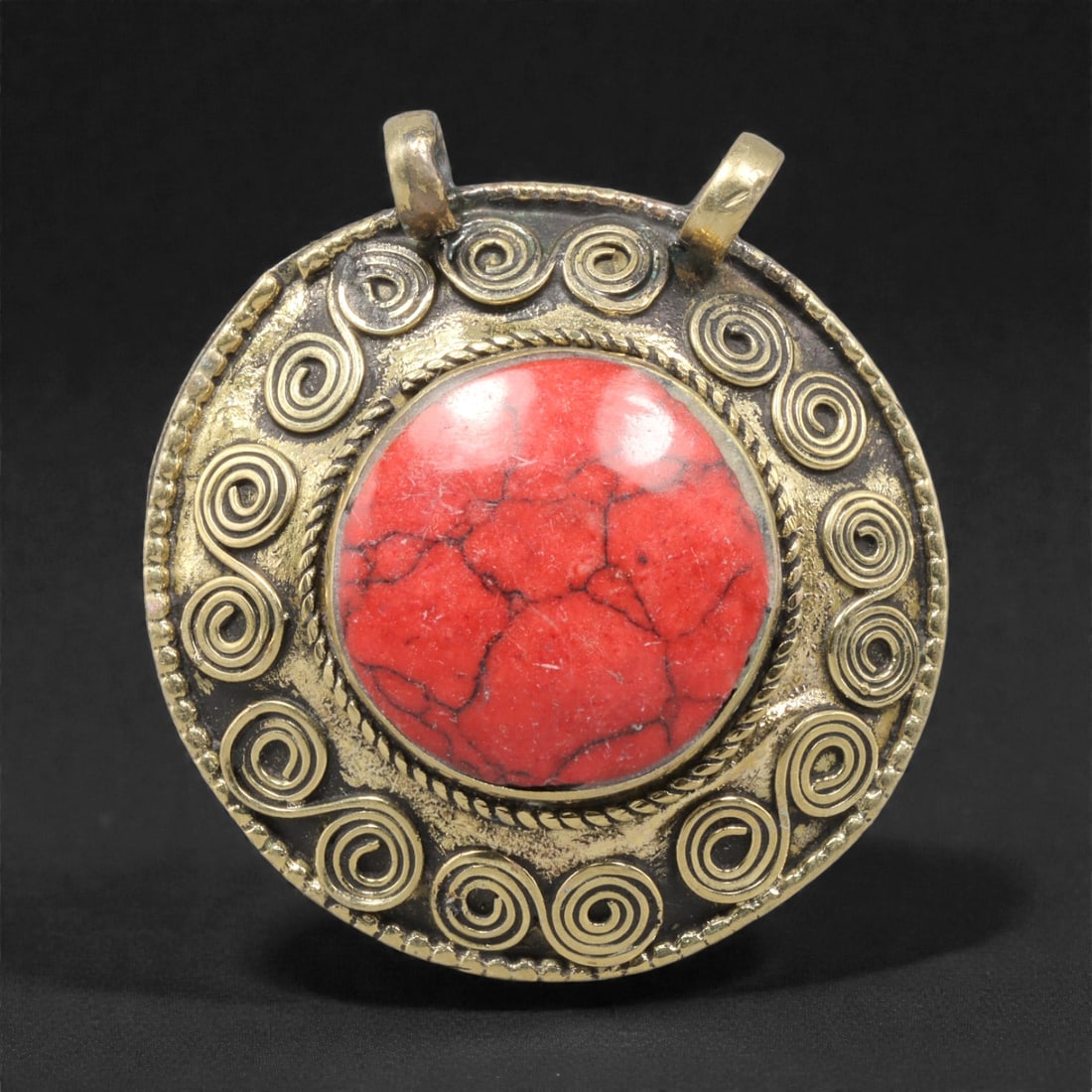 Himalayan Metal Pendant with Red Stone Inlay - Spiral-Motif Tribal Amulet, 66ZC: This round pendant features a prominent red stone cabochon set within a braided metal bezel, its vivid coloration contrasting strongly with the darker, textured background. Surrounding the central sto