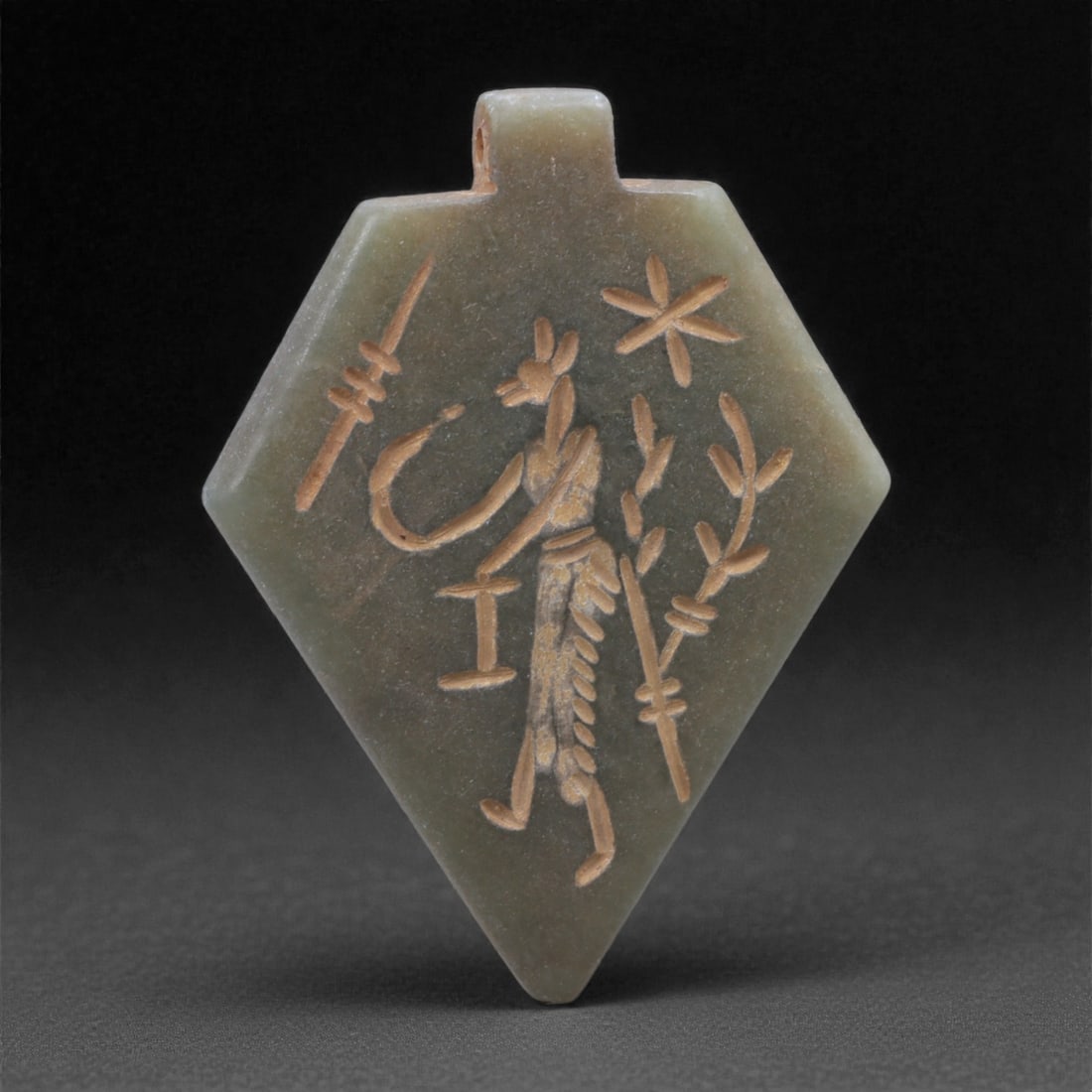 An Eastern Iranian Serpentine Amulet, Islamic Period, 9th-10th Century CE, 5cm, 78N: Carved from pale green serpentine with a smooth, slightly translucent surface, the object is worked in low relief on one face, with the reverse left plain and undecorated. The carved elements are defi