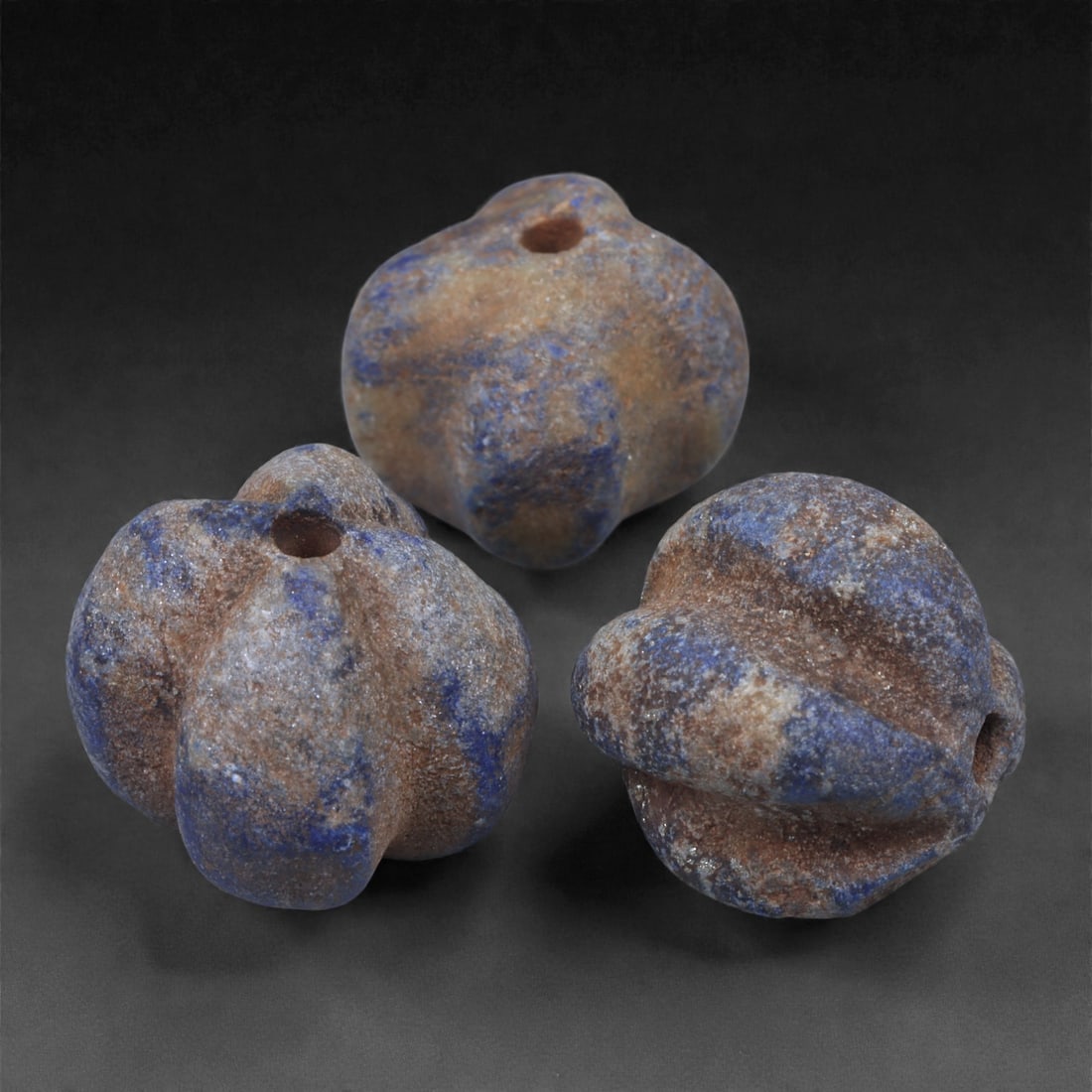 A Group of Three Egyptian Lapis Lazuli Melon Beads, 2nd Millennium BCE, 1.3-1.4cm, 8N: Carved from lapis lazuli with rich blue coloration interspersed with lighter calcite and brown mineral inclusions, the group comprises three melon-shaped beads of rounded, lobed form. Each bead is pie