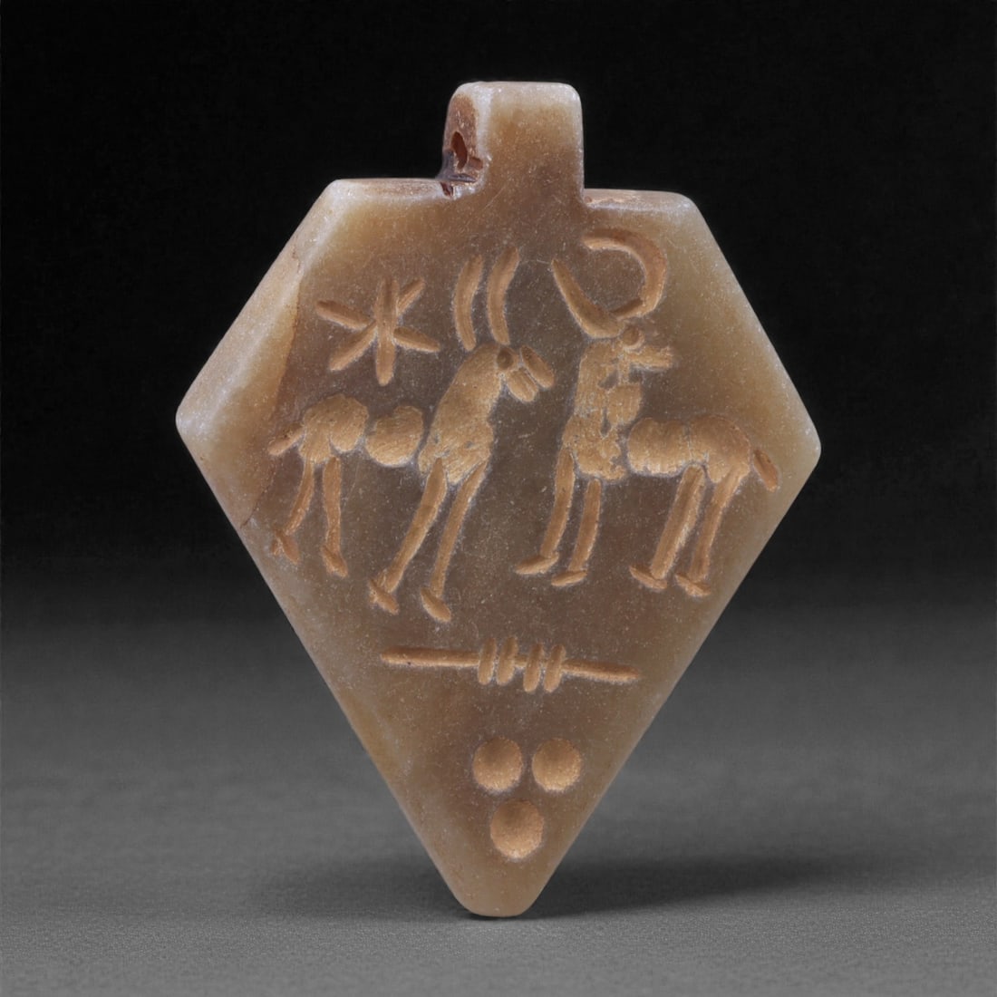 An Eastern Iranian Serpentine Amulet, Islamic Period, 9th-10th Century CE, 4.7cm, 81N: Carved from pale green serpentine with a smooth, slightly translucent surface, the object is worked in low relief on one face, with the reverse left plain and undecorated. The carved elements are defi