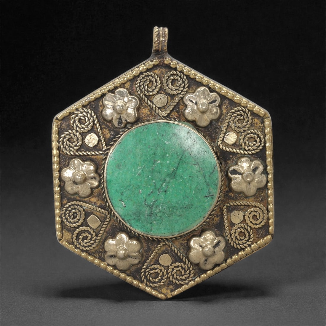 Himalayan Style Brass Pendant - Green Stone Floral, 22XF: This hexagonal brass pendant is organized around a large circular green stone cabochon set within a broad, slightly raised bezel. Surrounding the central stone are alternating floral appliques and coi