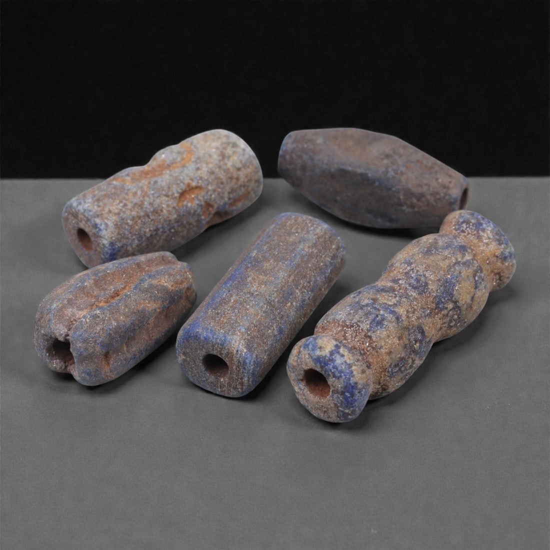 A Group of Five Near Eastern Lapis Lazuli Beads, 3rd Millennium BCE, 7N: Carved from lapis lazuli with mottled blue coloration and varying degrees of calcite and brown mineral inclusions, the group comprises five beads of differing cylindrical and sub-cylindrical forms. Ea