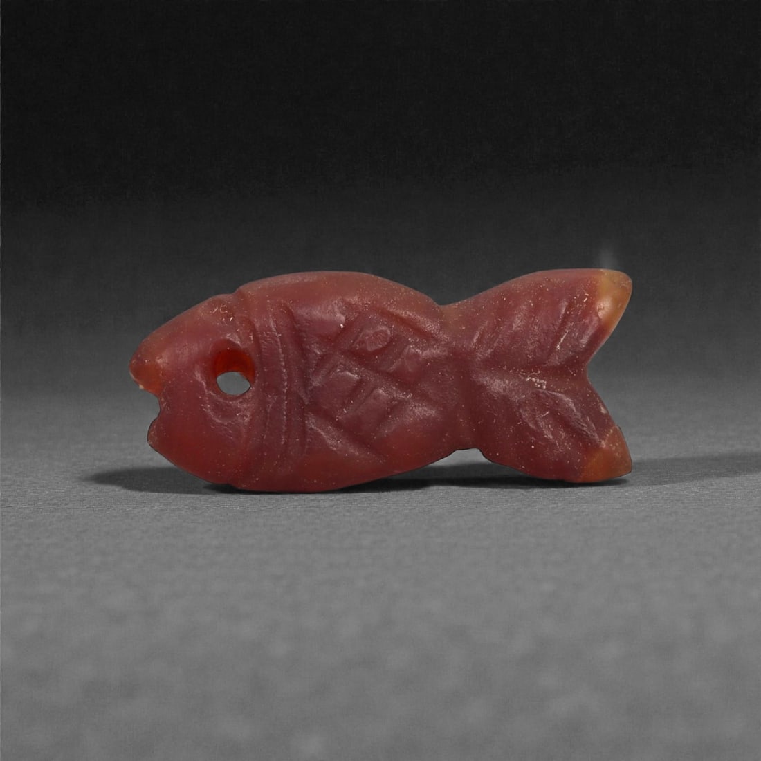 An Egyptian Carnelian Amulet, Coptic Period, 4th-7th Century CE, 2.1cm, 22LJ: Worked from orange carnelian with natural internal variation, the amulet shows a compact form with smoothed contours and modest surface definition. Light wear is visible along the edges. Objects of th