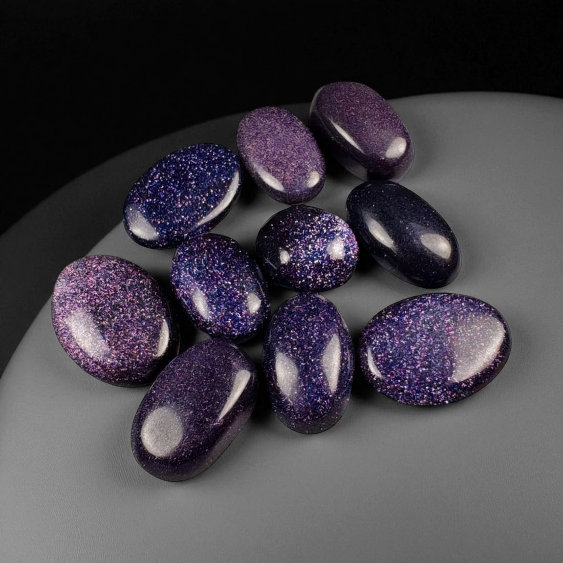 65.89 Carats Midnight Purple Goldstone Cabochon Selection Lot, 44WA: This radiant parcel of midnight purple goldstone cabochons shimmers with a captivating galaxy-like sparkle, each stone alive with fine metallic inclusions that dance beneath the surface. The deep viol