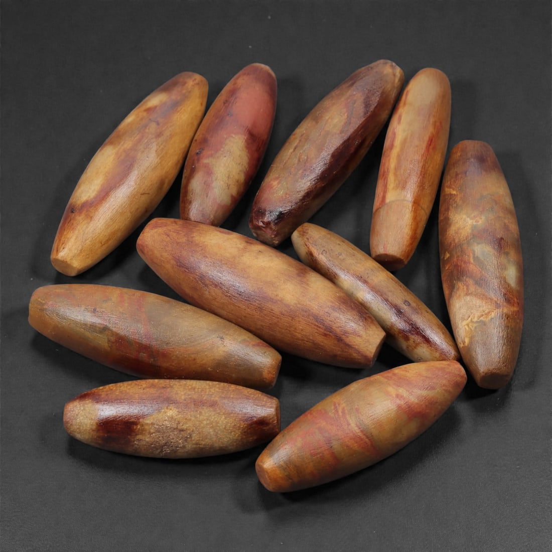 A Group of Indo-Tibetan Fossilized Wood Beads, Early 20th Century, 2.8-4cm, 31LN: Worked from dense fossilized wood, the group comprises spindle-shaped beads with smooth, polished surfaces displaying natural mineral inclusions and banding characteristic of silicified timber. Each b