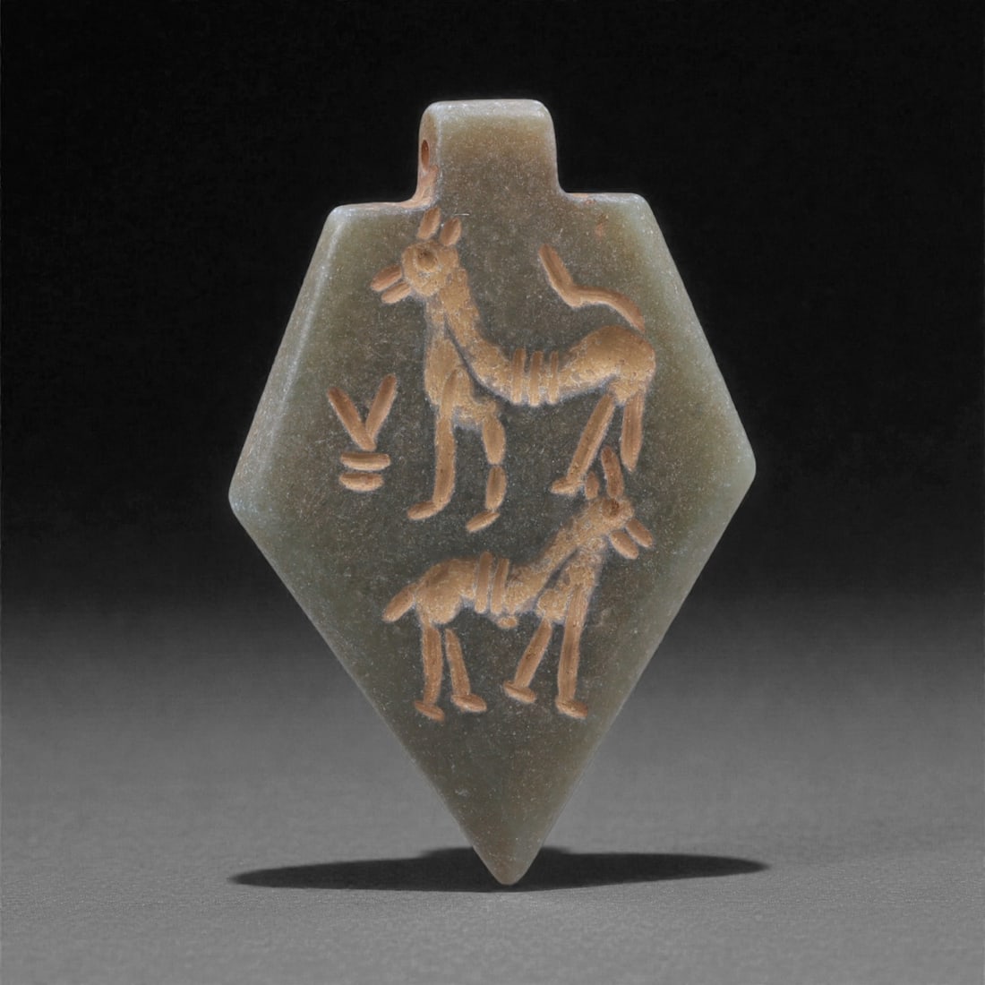 An Eastern Iranian Serpentine Amulet, Islamic Period, 9th-10th Century CE, 4.6cm, 43K: Carved from pale green serpentine with a smooth, slightly translucent surface, the object is worked in low relief on one face, with the reverse left plain and undecorated. The carved elements are defi