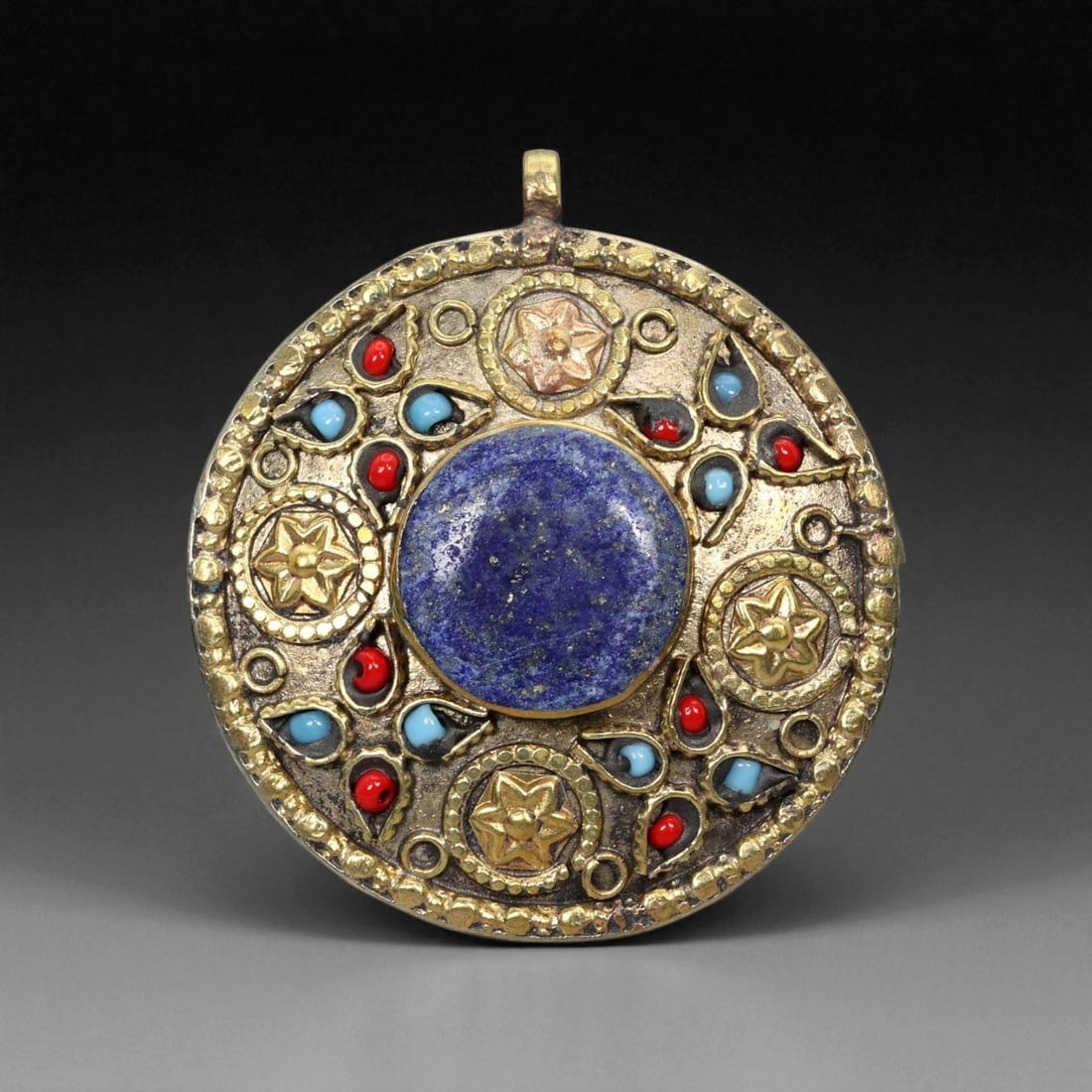 A Himalayan Tribal Lapis Lazuli Brass Pendant with Coral and Turquoise Inlay, 20th Century,, 85XD: This richly ornamented round pendant captures the vibrant aesthetic of Himalayan tribal jewelry, blending powerful color symbolism with intricate metal artistry. The centerpiece, a deep-blue lapis laz