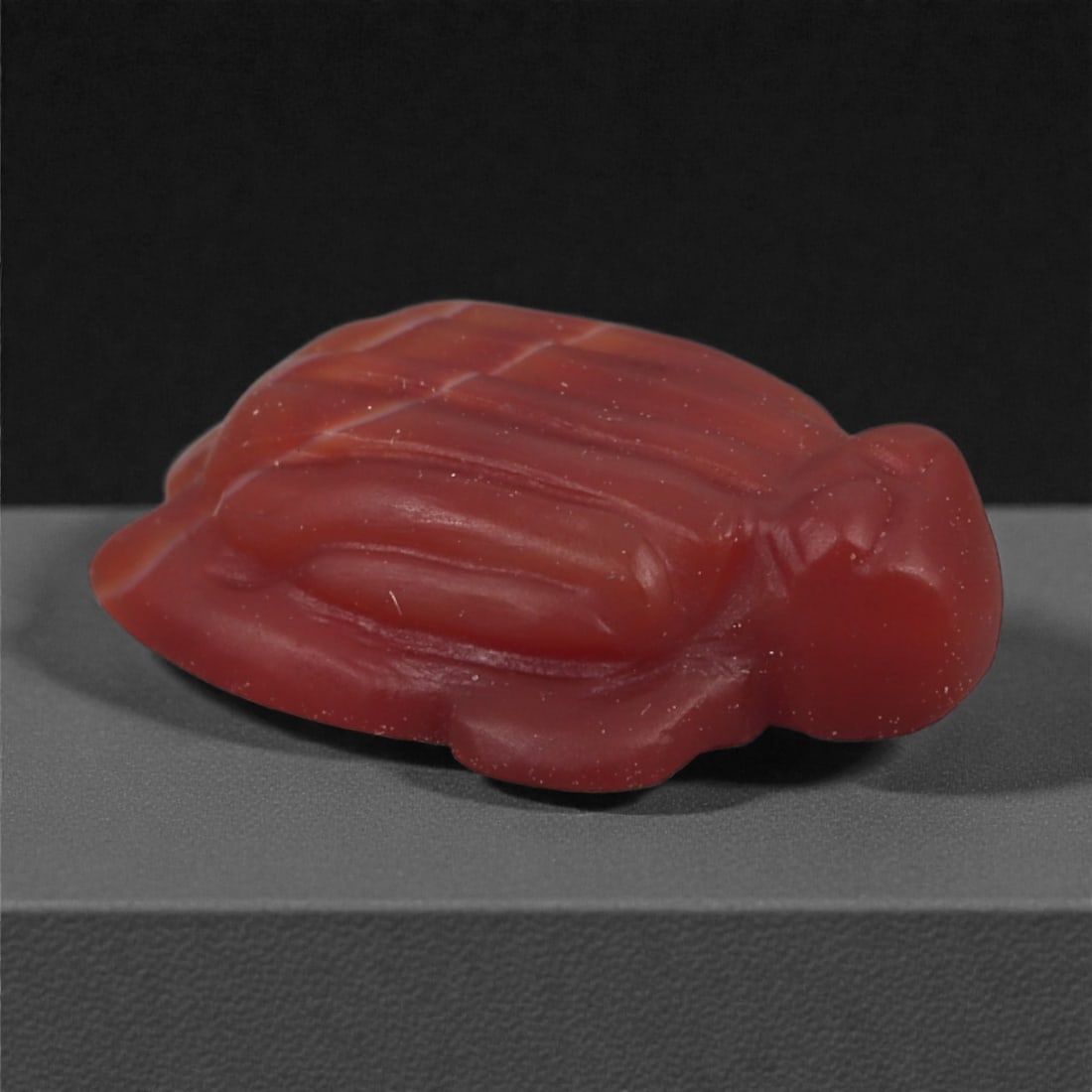 A Near Eastern Carnelian Turtle Amulet, 1st Millennium BCE, 44A: Carved from opaque red carnelian, the amulet depicts a turtle with a domed carapace defined by a series of parallel and cross-cut grooves. The head and limbs are rendered in a simplified manner, with 