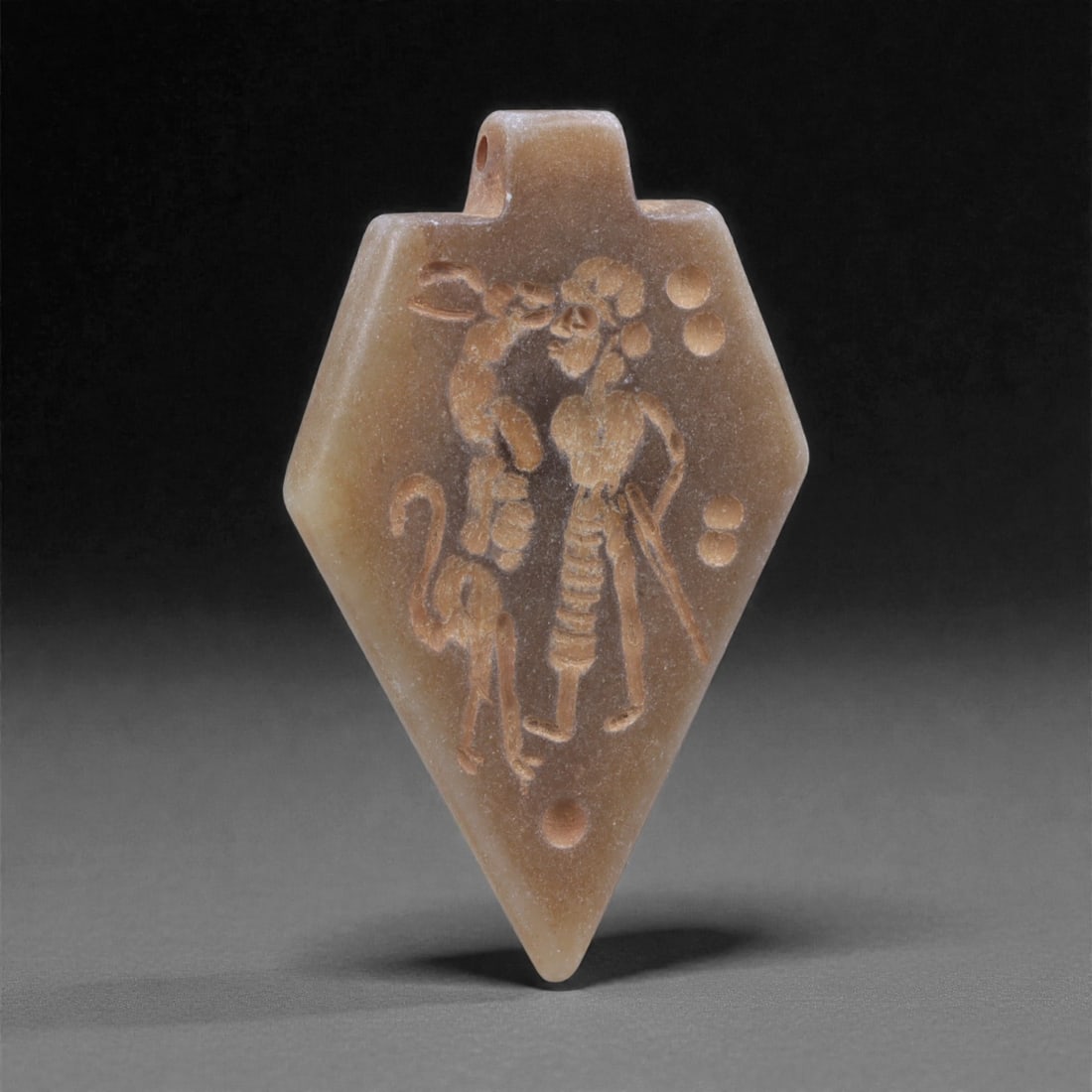 An Eastern Iranian Serpentine Amulet, Islamic Period, 9th-10th Century CE, 4.6cm, 13K: Carved from pale green serpentine with a smooth, slightly translucent surface, the object is worked in low relief on one face, with the reverse left plain and undecorated. The carved elements are defi