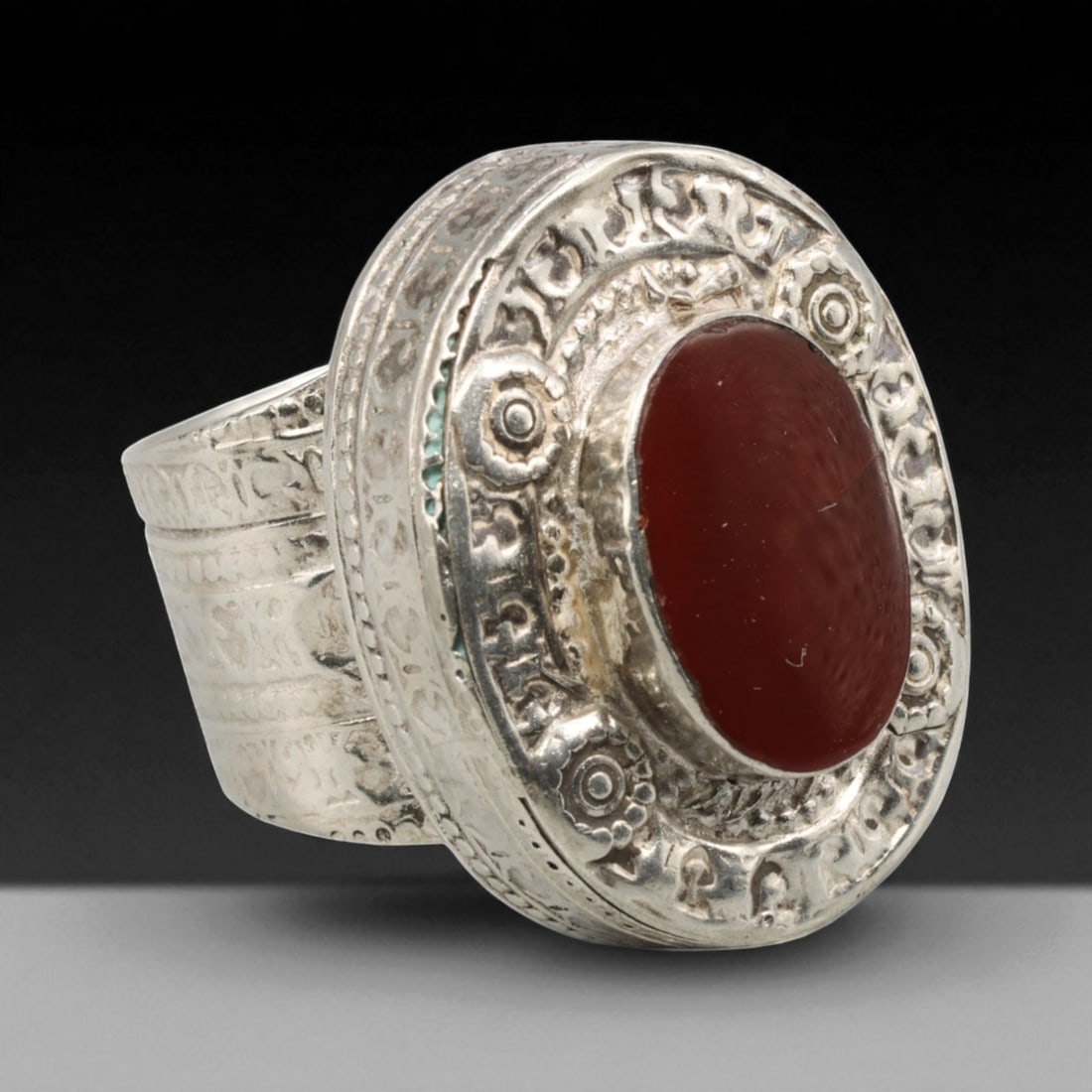 Antique Central Asian Carnelian Amulet Silver Ring, c. 19th-20th Century, US 9.5, 31BD: This commanding antique ring showcases the grandeur of Central Asian talismanic design, featuring an oval carnelian cabochon set within an elaborately engraved silver bezel. The ring's broad, circular