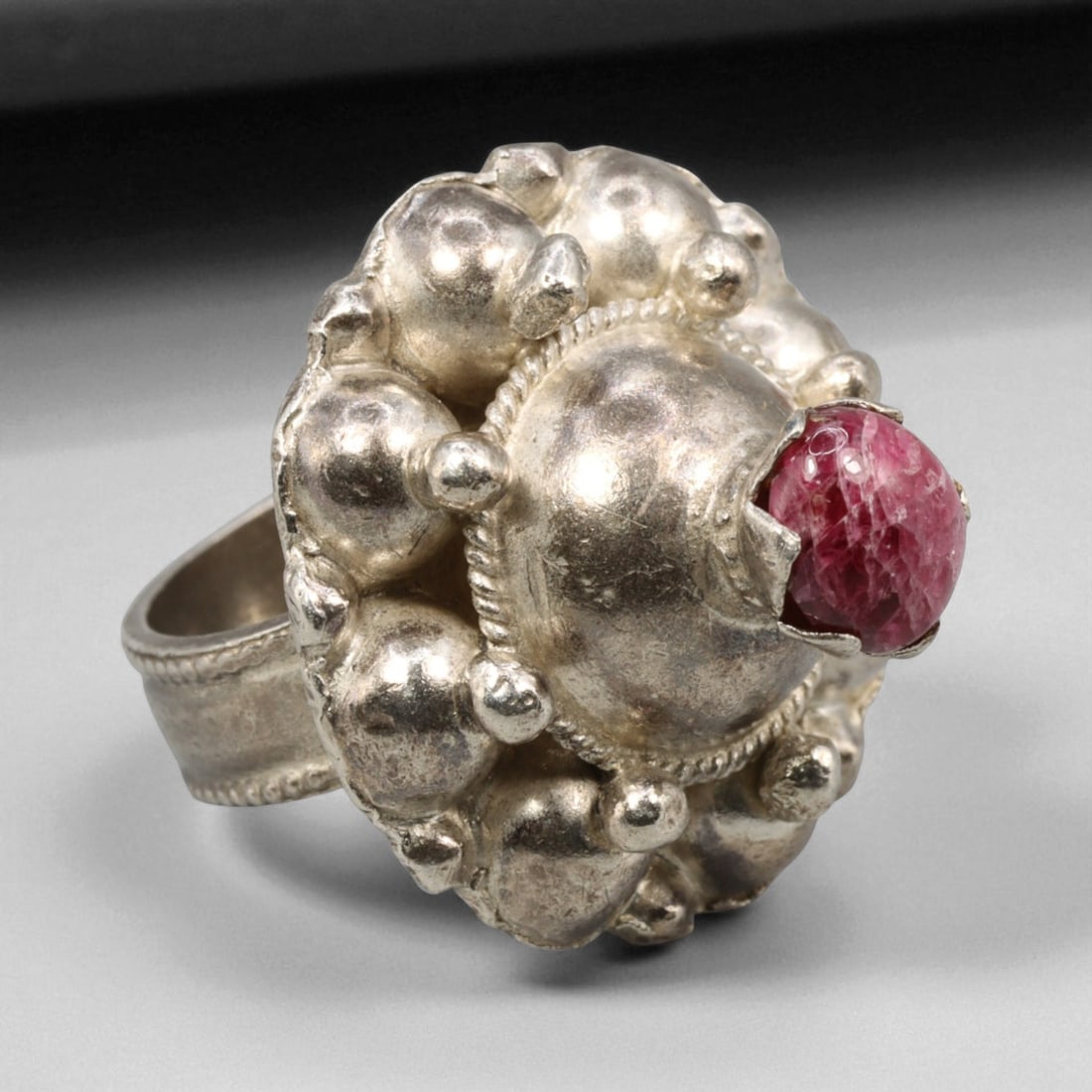 A Central Asian Granulated Silver Ring with Ruby Glass Cabochon, c. 19th-20th Century, 7 US, 13BD: This striking A ring showcases the bold elegance of Central Asian silversmithing from the late 19th to early 20th century. Crafted in high-relief repousse silverwork, it features a domed bezel surroun