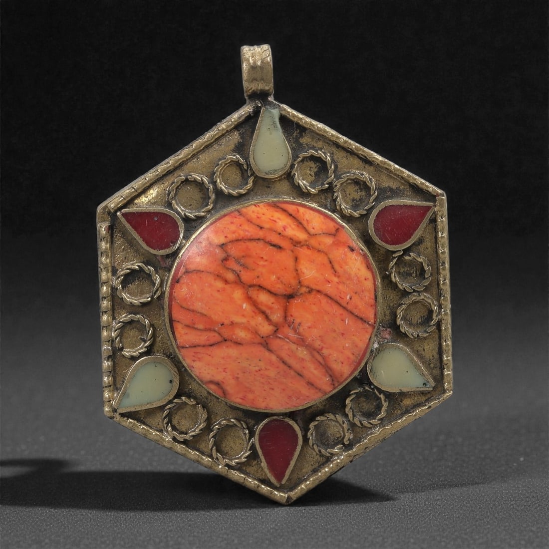 Buddhist Metal Pendant - Hexagonal Medallion with Orange Stone Inlay, 51ZC: This hexagonal metal pendant is centered on a large circular orange stone inlay exhibiting natural veining and a warm, mottled surface. Surrounding the central stone is a ring of raised metal wreath m