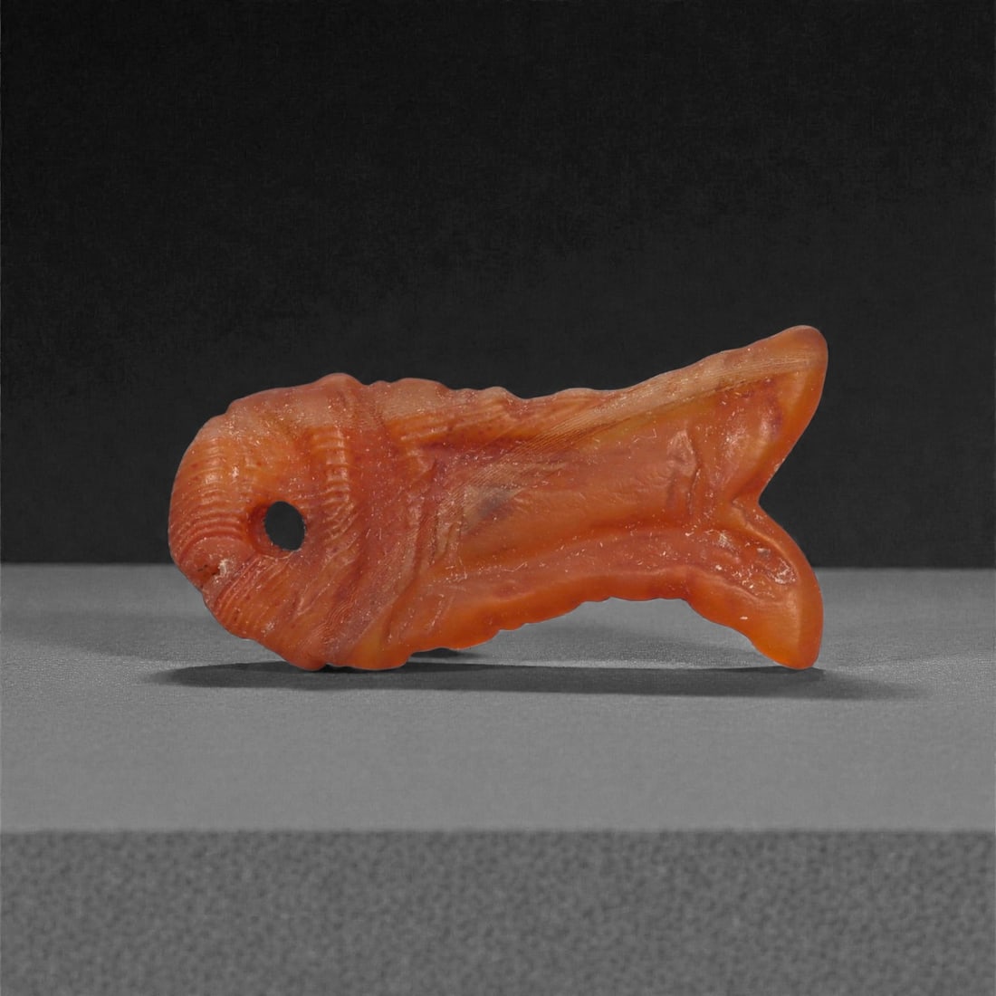 An Egyptian Carnelian Amulet, Coptic Period, 4th-7th Century CE, 2.3cm, 32LJ: Worked from orange carnelian with natural internal variation, the amulet shows a compact form with smoothed contours and modest surface definition. Light wear is visible along the edges. Objects of th