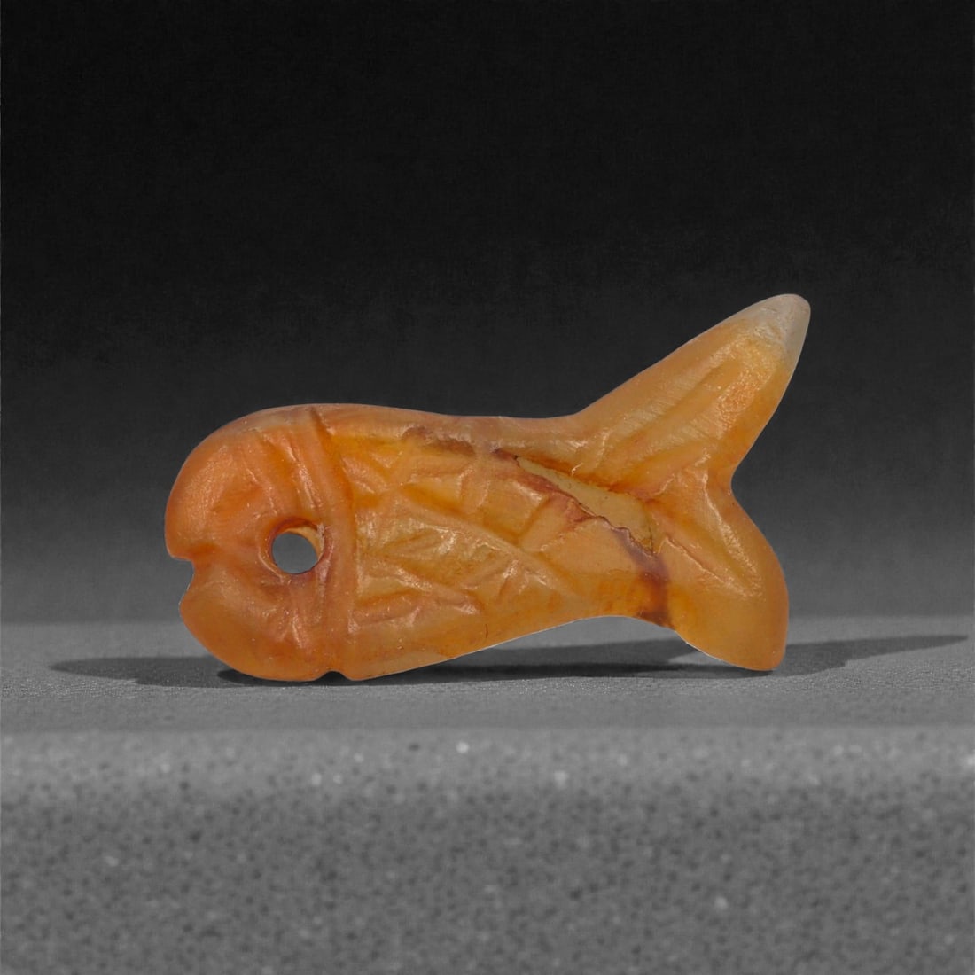 An Egyptian Carnelian Amulet, Coptic Period, 4th-7th Century CE, 2.5cm, 19LJ: Worked from orange carnelian with natural internal variation, the amulet shows a compact form with smoothed contours and modest surface definition. Light wear is visible along the edges. Objects of th
