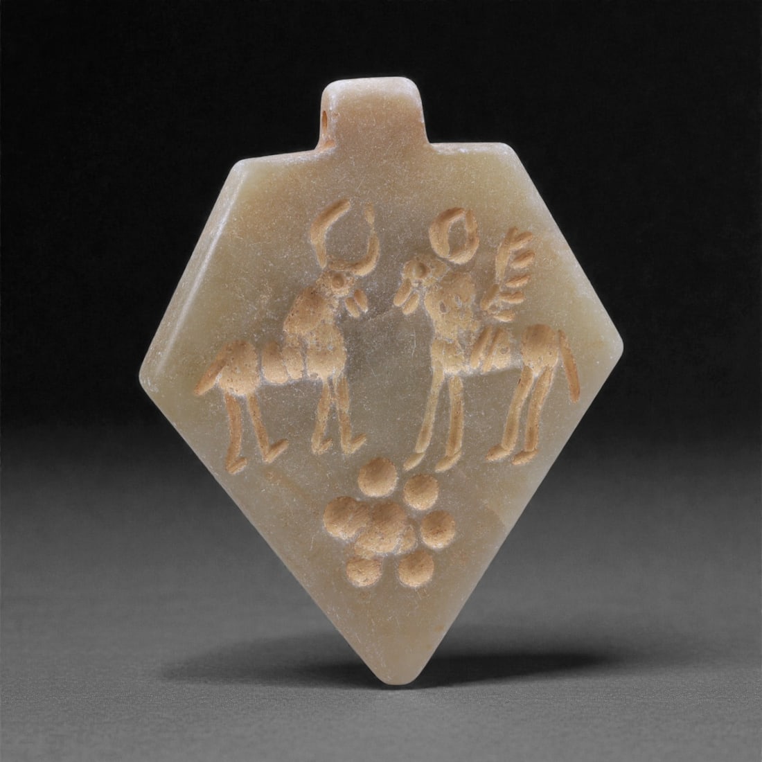 An Eastern Iranian Serpentine Amulet, Islamic Period, 9th-10th Century CE, 5cm, 67K: Carved from pale green serpentine with a smooth, slightly translucent surface, the object is worked in low relief on one face, with the reverse left plain and undecorated. The carved elements are defi