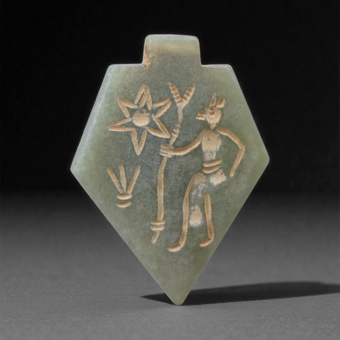 An Eastern Iranian Serpentine Amulet, Islamic Period, 9th-10th Century CE, 5cm, 23K: Carved from pale green serpentine with a smooth, slightly translucent surface, the object is worked in low relief on one face, with the reverse left plain and undecorated. The carved elements are defi