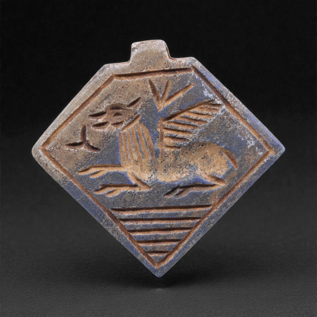 A Sasanian Lapis Lazuli Amulet, 3rd-7th Century CE, 4.5cm, 16Q: Carved from deep blue lapis lazuli with visible lighter inclusions and natural granular texture, the object is finished with a flat reverse and a front surface worked in low relief. The carving is exe