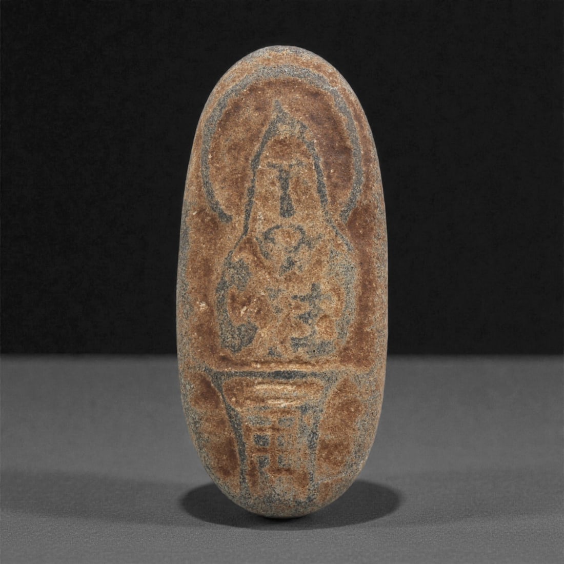 A Byzantine Stone Relief with Haloed Standing Figure, 10th-12th Century CE, 27ZC: Carved from a brown-grey stone with lighter surface abrasion, the object is shaped as an elongated oval plaque. The front bears a shallowly incised haloed figure, rendered with a tapered body and indi