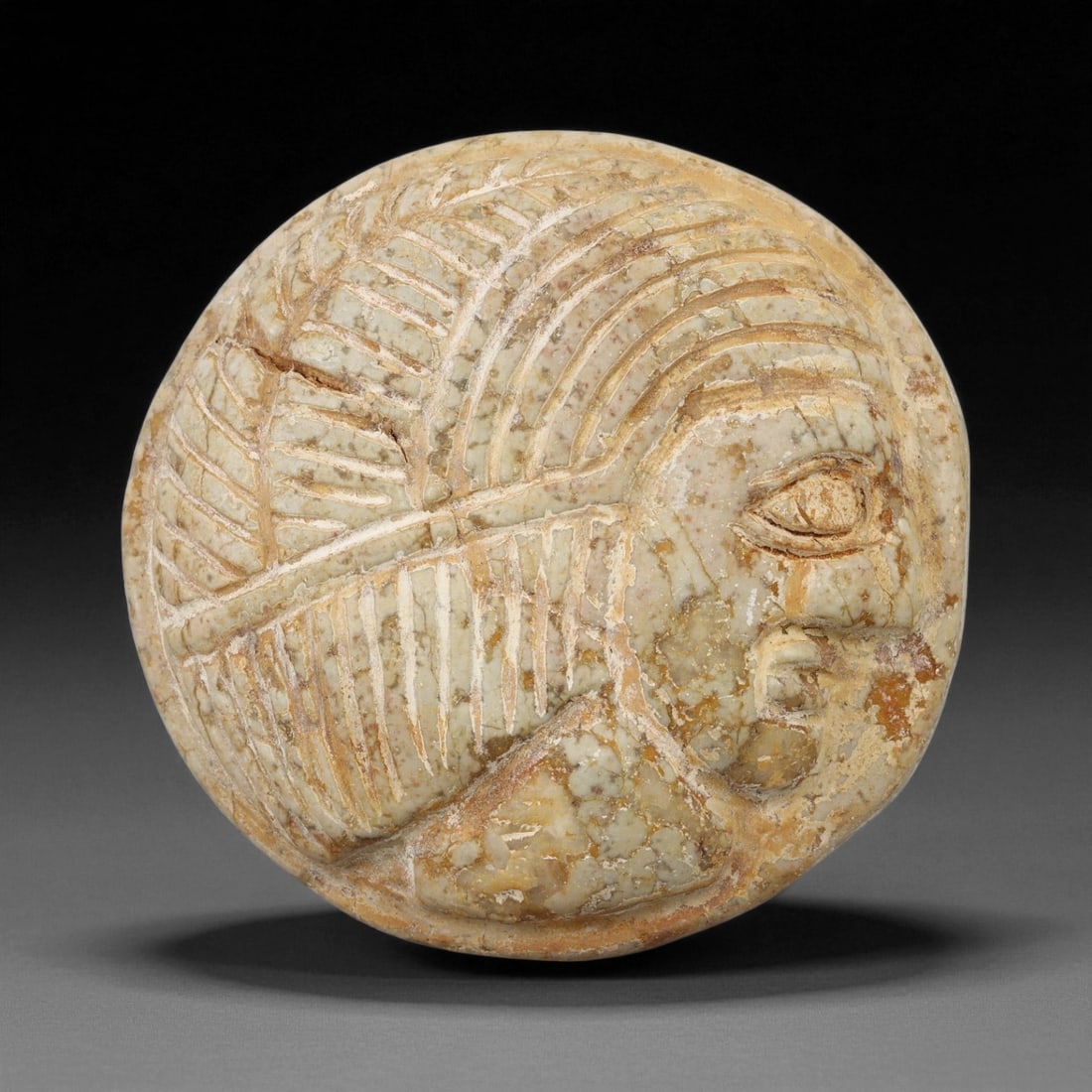 A Sasanian Stone Intaglio Plaque, 3rd-7th Century CE, 4.4cm, 54ES: The stone plaque is shaped with a convex surface bearing an incised profile head. The facial features are rendered with linear grooves defining the eye, brow, nose, and mouth, while additional incisio