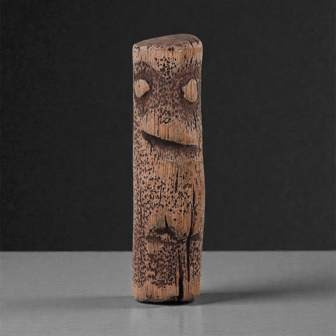 A Wooden Anthropomorphic Figurine, 19th-Early 20th Century, 43LG: Carved from light to medium brown hardwood with a coarse, porous grain, the figure is shaped as a tall cylindrical form with a slightly rounded top. The facial features are minimally indicated, includ