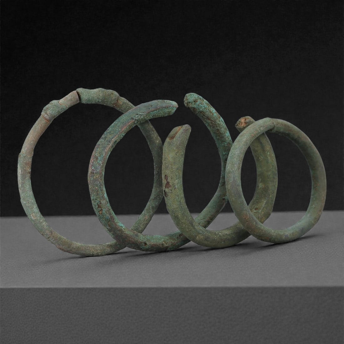 Roman Bronze Bracelets, 1st-3rd Century CE, 26H: Cast in bronze with rounded circular profiles, the group comprises four open bracelets exhibiting mottled green and brown patination with areas of surface accretion characteristic of burial conditions