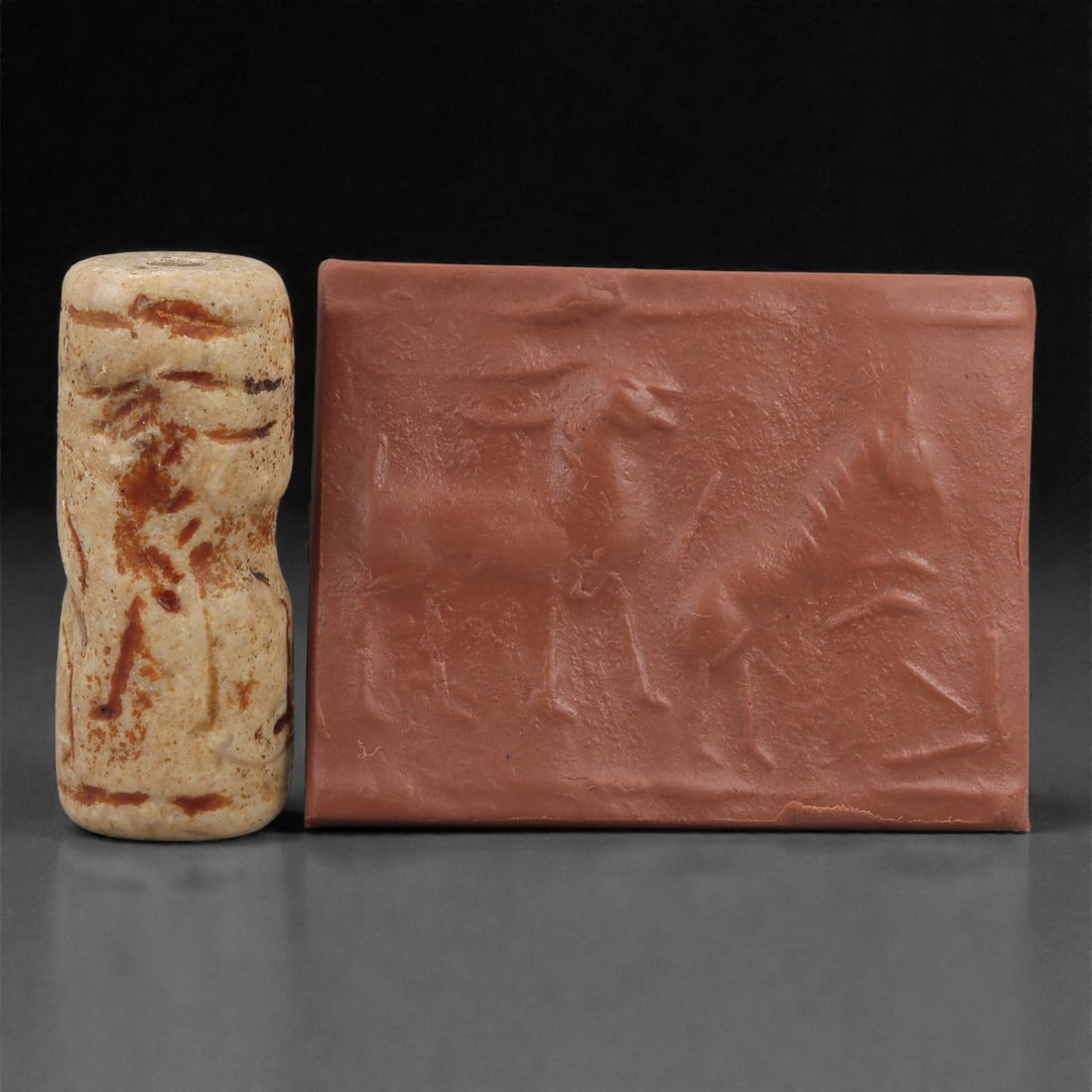 A Near Eastern Stone Cylinder Seal, 3rd Millennium BCE, 3.9cm, 88LM: Carved from stone with darker surface mottling, the cylindrical seal bears a continuous engraved scene. The carving is executed in shallow linear grooves typical of Early Bronze Age glyptic traditions