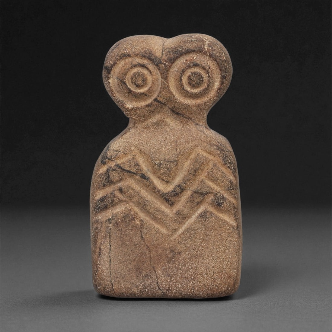 A Near Eastern Stone Eye Idol, 4th-3rd Millennium BCE, 85LB: Carved from a brown stone with natural surface veining, the object has a tapering rectangular body surmounted by a narrow neck and a bifurcated upper section. The head bears a pair of recessed circula