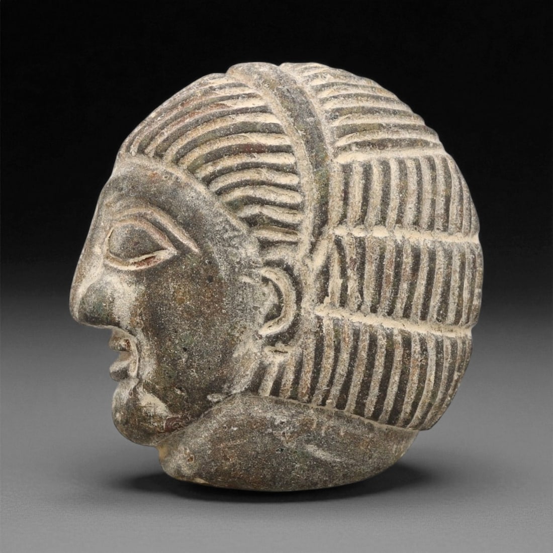 A Sasanian Stone Intaglio Plaque, 3rd-7th Century CE, 4cm, 64ET: The stone plaque is shaped with a convex surface bearing an incised profile head. The facial features are rendered with linear grooves defining the eye, brow, nose, and mouth, while additional incisio