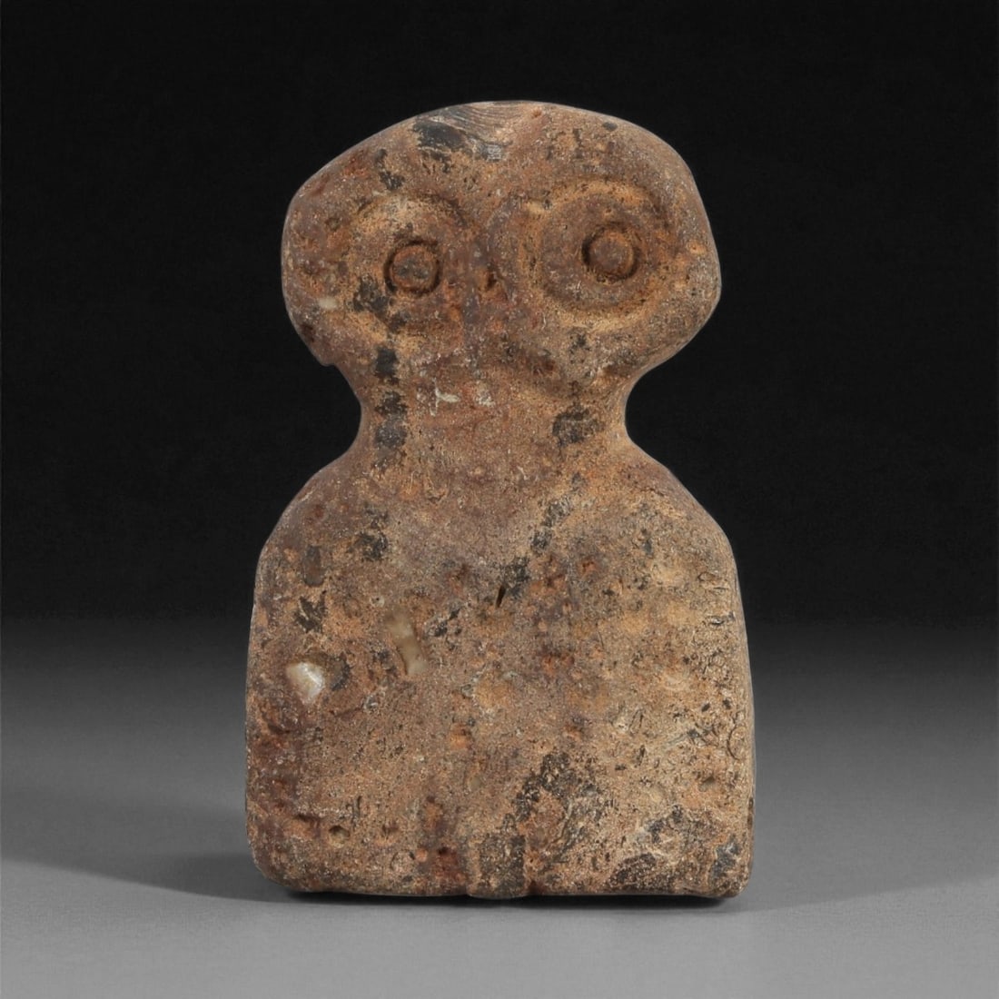 A Near Eastern Stone Eye Idol, 4th-3rd Millennium BCE, 33LG: Carved from a brown stone with scattered surface inclusions and areas of abrasion, the figure is rendered with a flat, rectangular lower body and a rounded upper section. The head bears a pair of rece