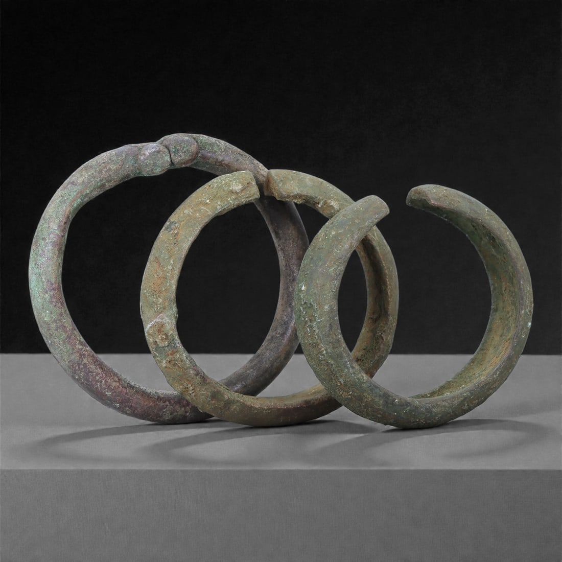 A Group of Roman Bronze Bracelets, 1st-3rd Century CE, 39H: Cast in bronze with a green and brown surface patina, the group comprises three open-ended bracelets of circular section. Each is shaped from a solid rod with slightly tapering terminals, one example