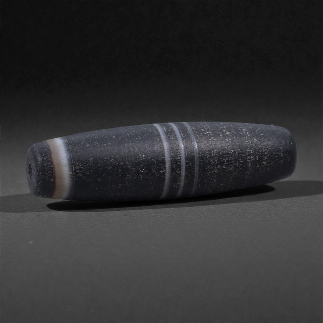 Antique Banded Agate Bead - Stone Amulet, 53Y: Carved from dark banded agate, this elongated bead exhibits naturally occurring pale linear bands running circumferentially across the surface, a characteristic feature of agate selected for personal