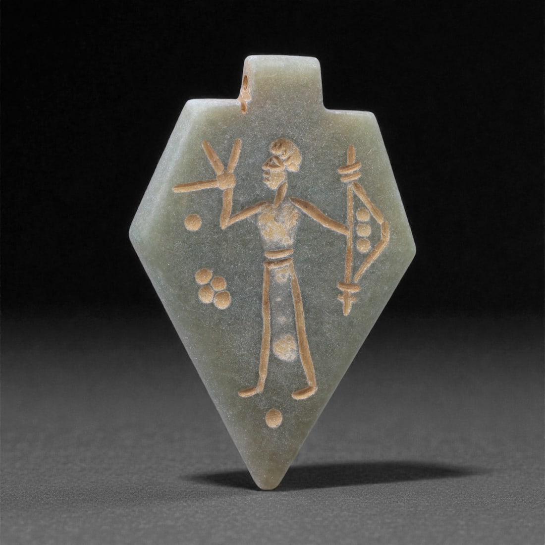 An Eastern Iranian Serpentine Amulet, Islamic Period, 9th-10th Century CE, 5.2cm, 6K: Carved from pale green serpentine with a smooth, slightly translucent surface, the object is worked in low relief on one face, with the reverse left plain and undecorated. The carved elements are defi