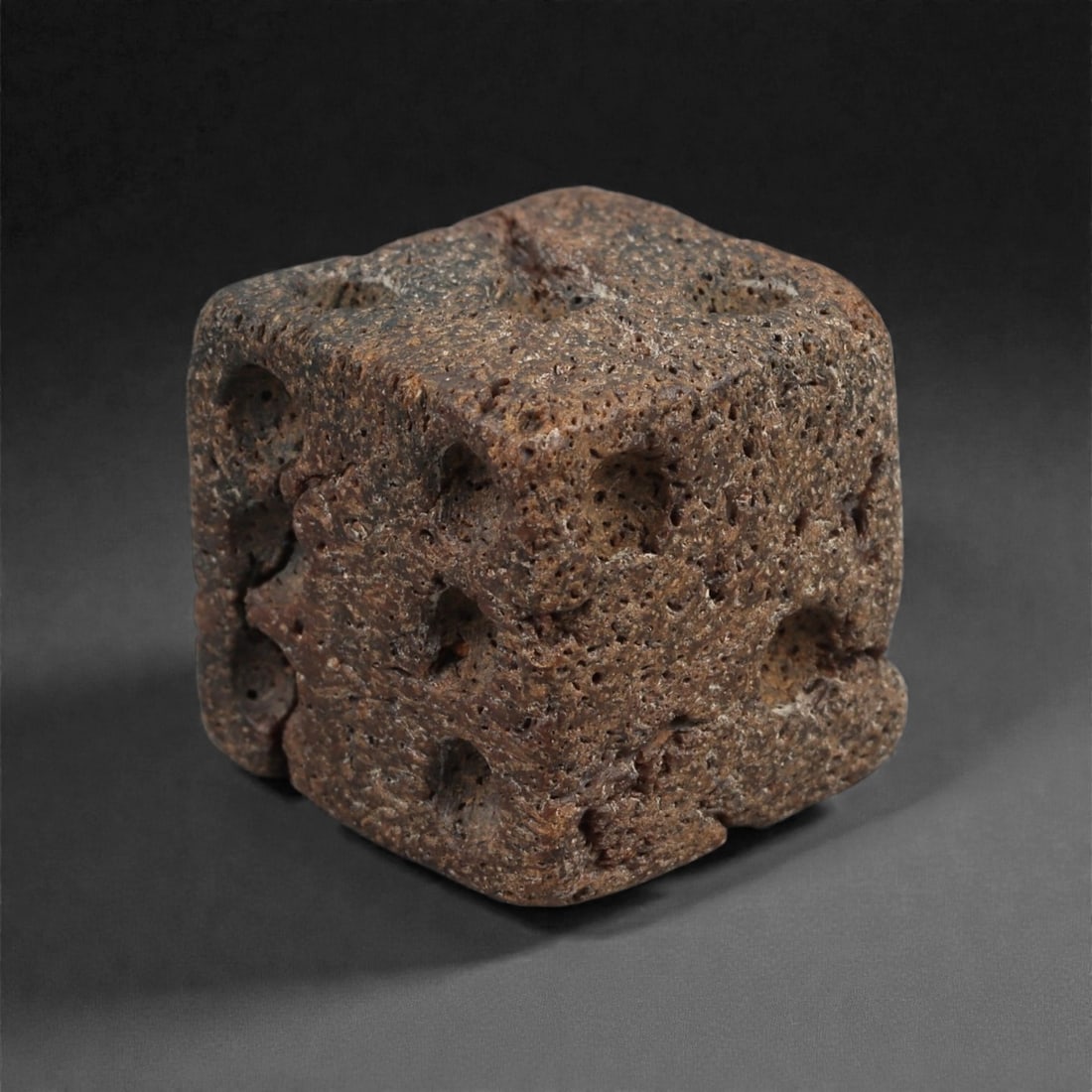 A Roman Bone Gaming Die, 1st-3rd Century CE, 1.5cm, 92AD: Carved from dense bone, the object is shaped as a small cube with slightly rounded edges. Each face bears a series of drilled circular pips arranged in standard numerical configurations. The surfaces 