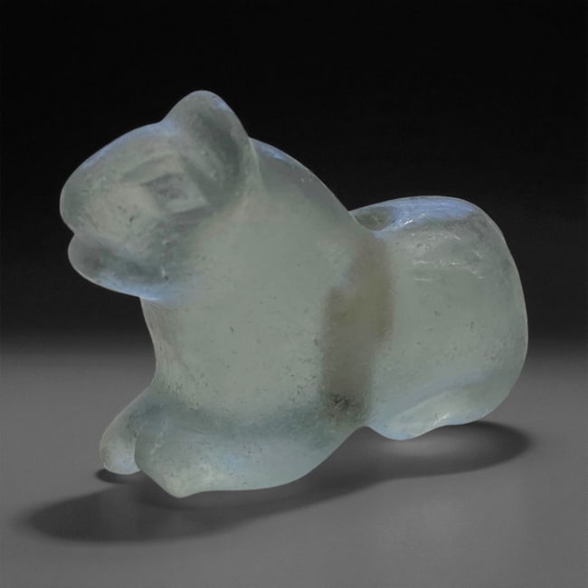 A Neo-Assyrian Rock Crystal Lion Amulet, 8th-7th Century BCE, 8LG: Carved from translucent rock crystal with minor internal inclusions, the amulet is shaped as a recumbent lion with a rounded body, short limbs tucked beneath, and a stylized head featuring a recessed 